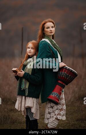 Eine junge Frau und ein Mädchen mit roten langen Haaren Kalimba und Trommel spielen in den Bergen im Herbst Stockfoto