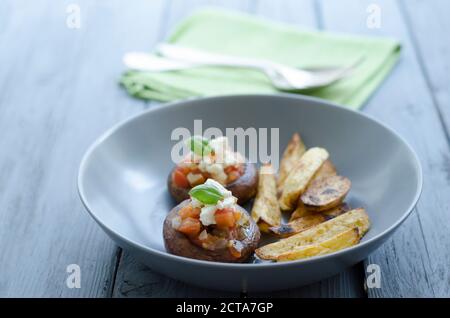 Schüssel von Pilzen mit Röstkartoffeln und Serviette auf Holztisch, Nahaufnahme Stockfoto