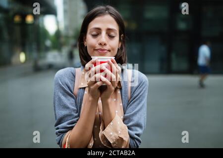 Fröhliche junge Frau, die nach dem Einkaufen in der Stadt Kaffee trinkt und mit Taschen spazieren geht. Stockfoto