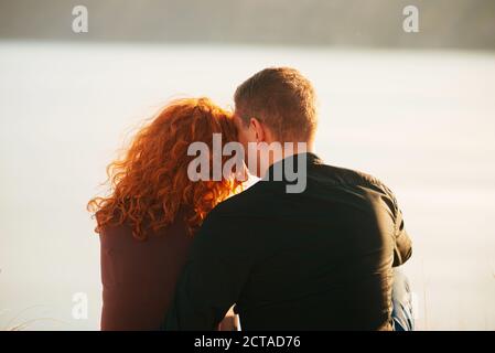 Ein junges nettes Paar, das nebeneinander sitzt und etwas Zeit zusammen in der Nähe eines Flusses hat. Stockfoto