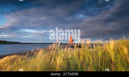 Ein stürmischer Abend mit Blick durch das Marram Gras & Sanddünen zum roten Leuchtturm und Pier in South Shields bei Sonnenuntergang. Stockfoto