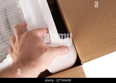 Verpackung von Waren in Karton mit Styropor-Material für den sicheren Transport der Ladung. Isoliert auf weißem Hintergrund. Die Hände des Mannes packen den Goo Stockfoto