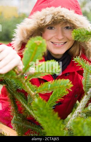 Blonde Frau in Winterkleidung schaut durch die Zweige der Ein Tannenbaum Stockfoto