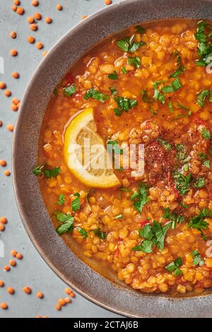 Rote Linsen Tomatensuppe mit Petersilie und Zitrone in grauem Teller auf Beton Tischplatte. Vegetarisches Gericht. Stockfoto