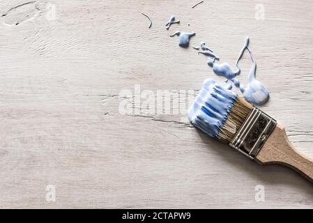 Ein blauer Pinsel liegt auf einem grauen Holzhintergrund Alt und Lackspritzer verschüttet Stockfoto