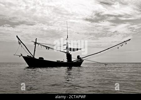 Schwarz-weiße Silhouette eines festgemachtes Fischerboot vor einem stürmisch bewölkten Himmel. Stockfoto