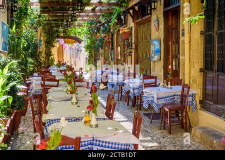 Tische und Stühle unter Schatten in einer griechischen Taverne in den Seitenstraßen der Altstadt von Rhodos, Dodekanes, Griechenland Stockfoto