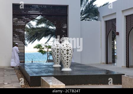 Ein Omani in seinem dishdasha, der am Hafen vorbei läuft. Wasserspiele mit Springbrunnen. Al Mouj, die Welle, Maskat, Sultanat von Oman. Stockfoto