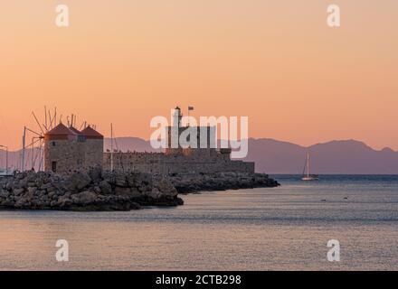 Rhodos Sonnenuntergang über St. Nicholas Festung und die Windmühlen säumen die äußere Anlegestelle von Mandraki Hafen, Rhodos Stadt, Rhodos Insel, Griechenland Stockfoto