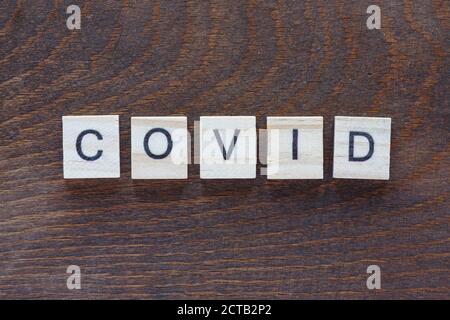 Geschrieben 'COVID' mit hellen Holzbuchstaben auf dunklem Holz Stockfoto