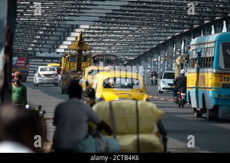 Kolkata, Indien - 2. Februar 2020: Gelbe klassische Taxis, öffentliche Verkehrsmittel Busse und Motorradfahrten nicht identifizierte Fußgänger überqueren Howrah Brücke Stockfoto