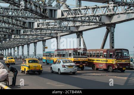 Kolkata, Indien - 2. Februar 2020: Gelbe klassische Taxis, bunte öffentliche Verkehrsmittel Busse und Autos fahren über Howrah Brücke am 2. Februar 2020 Stockfoto