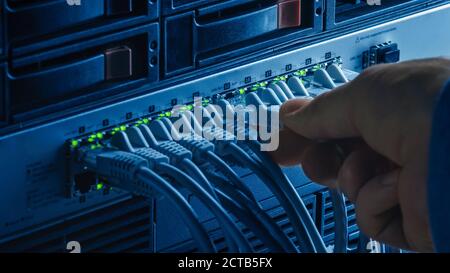 Makroaufnahme: Person wird in RJ45 Internet Connector in LAN Router Switch eingestöpsel. Informationskommunikationsnetzwerk mit Datenkabeln, die an den Modemanschluss angeschlossen sind Stockfoto