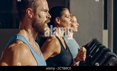 Aufnahme des athletischen Mannes, der auf dem Laufband läuft und Fitnessübungen macht. Sportliche und muskulöse Frauen und Männer aktiv Training in der modernen Turnhalle. Seitenansicht Stockfoto