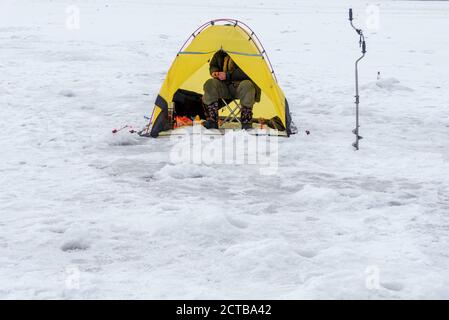 Eisfischen im gelben Zelt. Mann Eisfischen auf einem gefrorenen See im Zelt. Winterurlaub und Menschen Konzept. neva Fluss.. Stockfoto