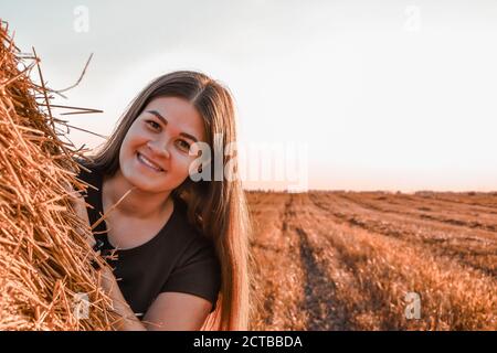 Porträt von jungen glücklich lächelnden Frau auf dem Heuhaufen in Sonnenuntergang, Land. Das Konzept der Freiheit der Entdeckungsfreude und der frischen Luft in der Natur Stockfoto