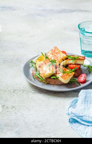 Gebratenes Halloumi-Sandwich mit Rucola und Tomaten auf einem grauen Teller. Toast mit gegrilltem Käse und Tomaten. Stockfoto