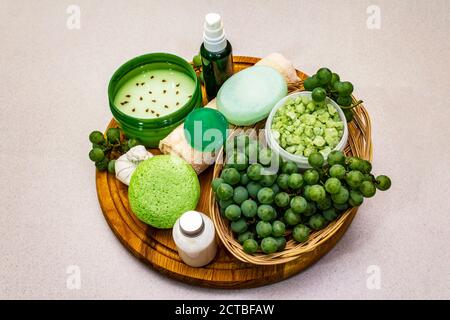 Natürliche Spa-Accessoires und grüne Trauben auf einem Holzteller platziert. Frische Zutaten für eine gesunde und komfortable Selbstpflege. Steinbeton Hintergrund, Stockfoto