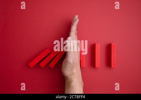 Rote Domino Blöcke, die zu fallen beginnt und eine Hand, die es vom Fallen verhindert. Stockfoto