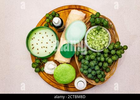 Natürliche Spa-Accessoires und grüne Trauben auf einem Holzteller platziert. Frische Zutaten für eine gesunde und komfortable Selbstpflege. Steinbeton Hintergrund, Stockfoto