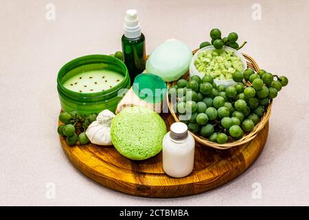 Natürliche Spa-Accessoires und grüne Trauben auf einem Holzteller platziert. Frische Zutaten für eine gesunde und komfortable Selbstpflege. Steinbeton Hintergrund, Stockfoto