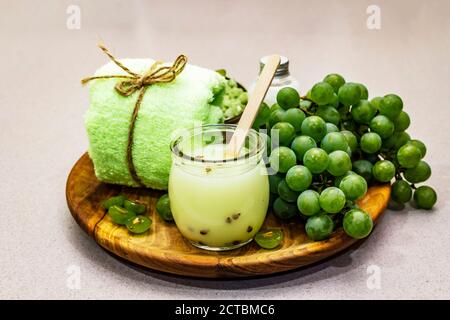 Natürliche Spa-Accessoires und grüne Trauben auf einem Holzteller platziert. Frische Zutaten für eine gesunde und komfortable Selbstpflege. Steinbeton Hintergrund, Stockfoto