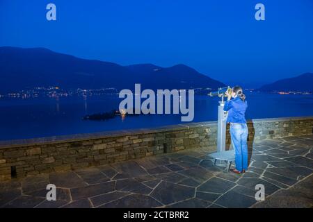 Frau mit Teleskop in Blue Hour und Brissago iIlands am Alpinen Lago Maggiore mit Berg im Tessin, Schweiz. Stockfoto