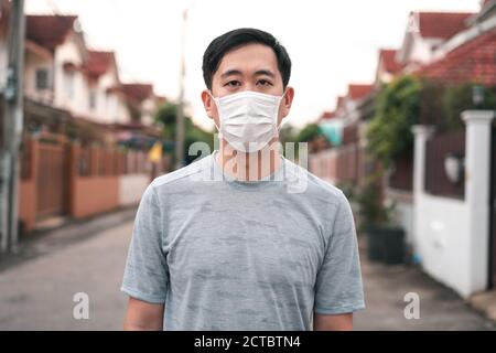 Junger asiatischer Mann trägt eine Gesichtsschutzmaske vor seinem Haus im Freien. Tragen einer Gesichtsmaske vor dem Verlassen des Hauses. Stockfoto