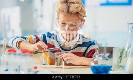 Grundschule Wissenschaft oder Chemie Klassenzimmer: Smart Little Boy tragen Schutzbrille mischt Chemikalien in Bechergläser Stockfoto