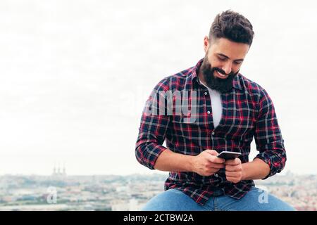 Porträt eines schönen bärtigen Mann tippt eine Textnachricht auf seinem Handy, Konzept der Freiheit und Technologie, kopieren Raum für Text Stockfoto