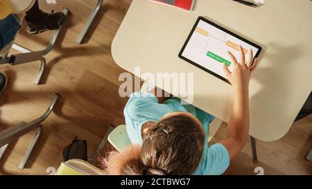 Draufsicht Aufnahme in der Grundschule Computer Science Classroom: Kinder sitzen an ihrem Schreibtisch mit Personal-Computern und digitalen Tablets für Stockfoto