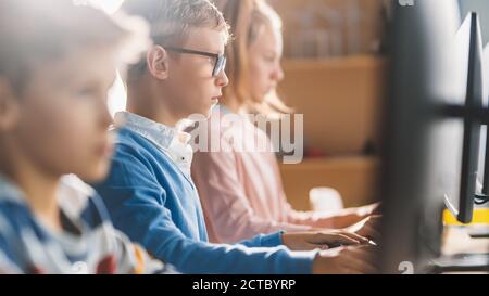 Grundschule Wissenschaft Klassenzimmer: Intelligente kleine Schüler sitzen in Reihe und arbeiten an Personal Computers, lernen Programmiersprache für Stockfoto