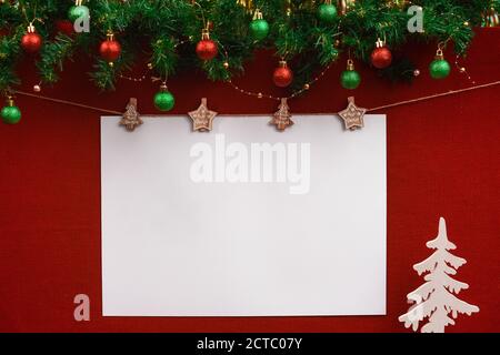 Weihnachtliches Layout mit weißem, unbeschriftetem Lettering-Blatt auf rotem Stoff Hintergrund mit Weihnachtsschmuck und Spielzeugbaum Stockfoto