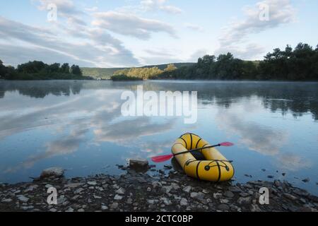 Gelbes Packfloß Gummiboot mit roter Pfanne auf einem Sunrise River. Packrafting. Aktives Lebenskonzept Stockfoto