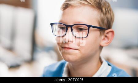 Porträt eines niedlichen kleinen Jungen trägt Brille, sitzt an seinem Schultisch, Smiles glücklich. Smart Little Boy mit Charming Smile sitzt in der Stockfoto
