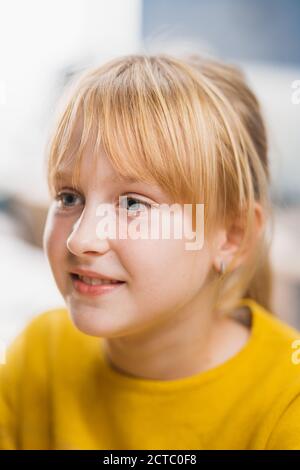 Portrait eines niedlichen kleinen Mädchens mit blondem Haar, das an ihrem Schultisch sitzt, smiles happily. Smart kleines Mädchen mit charmanten Lächeln sitzt in der Stockfoto