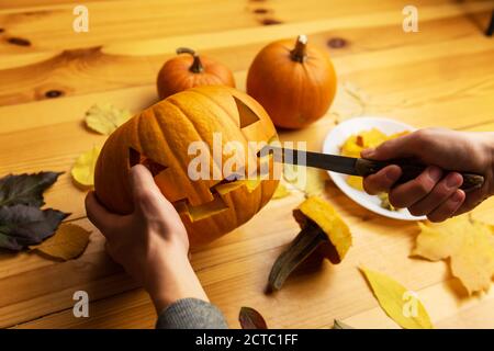 Halloween Schnitzen. Nahaufnahme von Kinderhänden mit Kürbis oder Jack-o-Laterne und Messer zu Hause. Dekoration und Urlaub Konzept Stockfoto