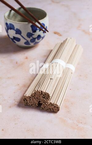 Drei Bündel trockener japanischer Soba-Nudeln mit einer leeren Nudel-Keramikschale und hölzernen Essstäbchen. Stockfoto