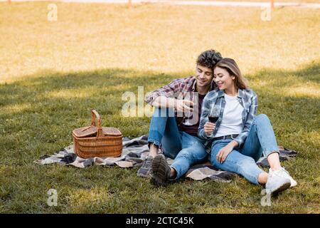 Pärchen sitzt auf karierten Decken und hält rote Gläser Wein Stockfoto