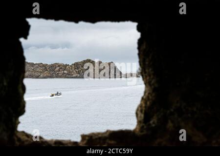 Ein Blick auf Shipman's Head auf Bryher, mit einem Boot vorbei, gesehen durch eine Lücke in Cromwell's Castle auf Tresco, Isles of Scilly Stockfoto