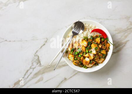 Fischcurry mit grünen Erbsen und Spinat serviert mit Reis in einer weißen Schüssel auf einem Marmortisch, Landschaftsansicht von oben, flach liegend, Freiraum Stockfoto