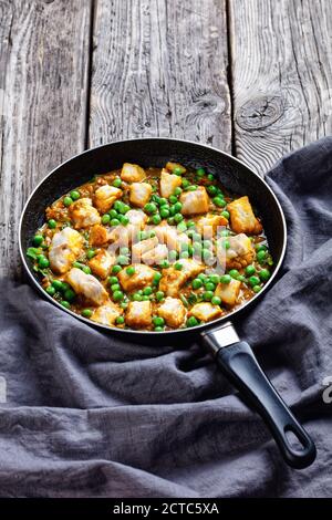 Heißer Kabeljau Fisch Curry mit grünen Erbsen und Spinat in einer Pfanne auf einem dunklen Holz rustikalen Tisch mit grauem Tuch, vertikale Ansicht von oben Stockfoto