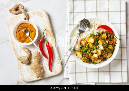 Fischcurry mit grünen Erbsen und Spinat serviert mit Reis in einer weißen Schüssel auf einem Marmortisch mit Zutaten, Landschaftsansicht von oben, flach liegend, frei Stockfoto