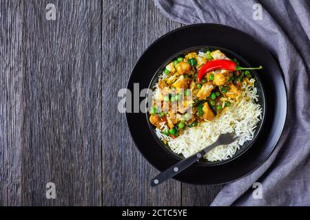 Fischcurry mit grünen Erbsen und Spinat serviert mit Reis in einer schwarzen Schüssel auf einem Holztisch, Landschaftsansicht von oben, flach liegend, Freiraum Stockfoto