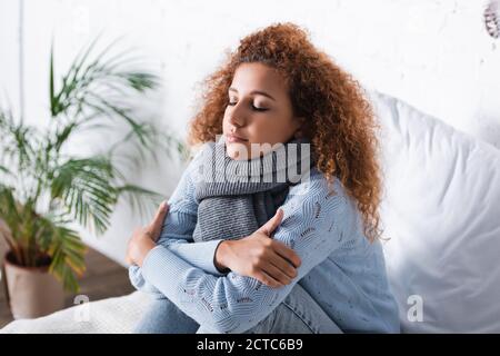 Rothaarige Frau in Schal und Pullover fühlen sich kalt auf Bett Stockfoto