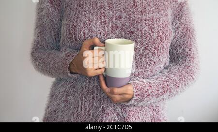 Eine Frau in einem zotteligen Pullover hält eine Tasse Kaffee oder Tee. Stockfoto