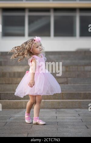 Kleines Mädchen in rosa Kleid Spinnen herum auf der Straße Stockfoto