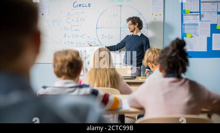 Fürsorglicher Lehrer erklärt Lektion zu einem Klassenzimmer voller heller vielfältiger Kinder. In der Grundschule mit Gruppe von intelligenten multiethnischen Kinder lernen Stockfoto