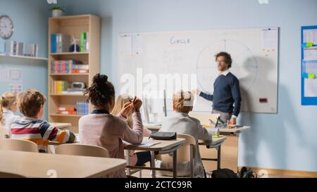 Fürsorglicher Lehrer erklärt Lektion zu einem Klassenzimmer voller heller vielfältiger Kinder. In der Grundschule mit Gruppe von intelligenten multiethnischen Kinder lernen Stockfoto