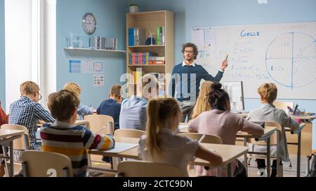 Fürsorglicher Lehrer erklärt Lektion zu einem Klassenzimmer voller heller vielfältiger Kinder. In der Grundschule mit Gruppe von Smart Multiethnic Learning Science Stockfoto